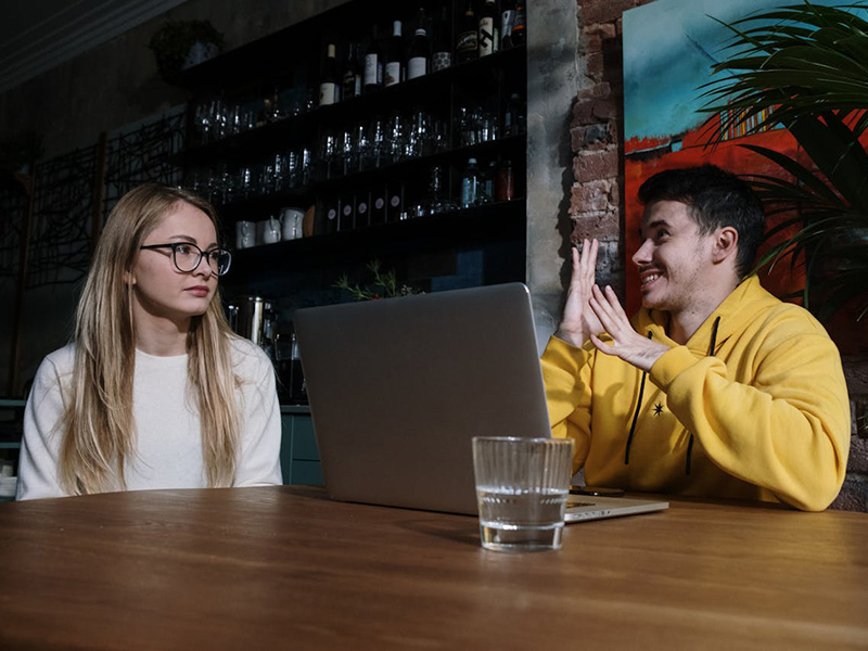 Young man with laptop and glass of water, chatting with young woman in bar