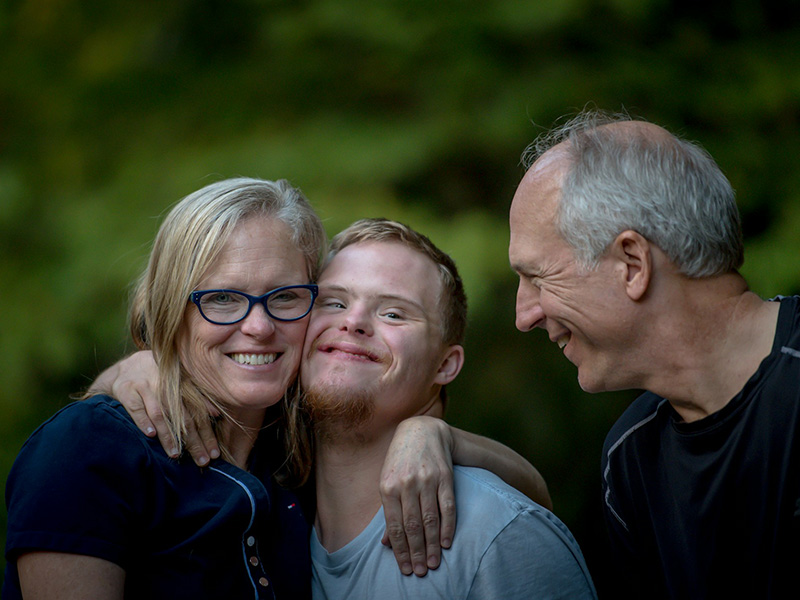 Smiling family portrait: mother with arm round teenage boy while father looks on