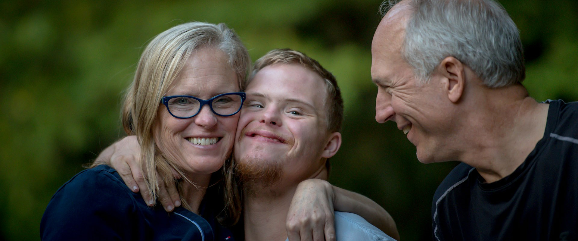 Smiling family portrait: mother with arm round teenage boy while father looks on